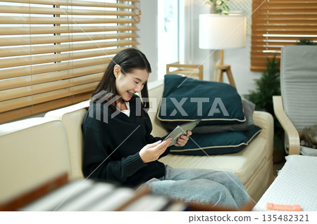 A young woman relaxing on a sofa using a tablet at home, enjoying a calm holiday mood with comfort and leisure time A young woman relaxing on a sofa using a tablet at home, enjoying a calm holiday mood with comfort and leisure time 135482321