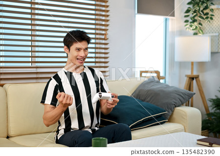 A man celebrates with joy while playing video games in his living room at home 135482390