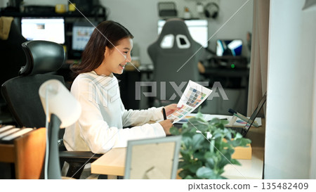 Female graphic designer working on logo creation with drawing tablet and color palette in modern bright office. Female graphic designer working on logo creation with drawing tablet and color palette in modern bright office. 135482409