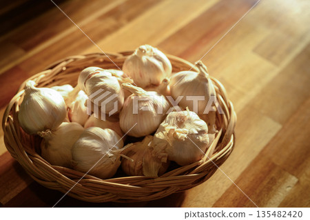 Fresh garlic bulbs in a woven basket on a wooden table 135482420