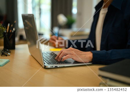 Cropped shot man writing on sticky notes and using laptop computer at a modern workspace, with multitasking concept 135482452