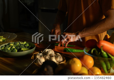 Cropped shot Man slicing green chili on a wooden board in a kitchen 135482460