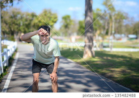 A Man stopping to rest after running on a park road 135482488