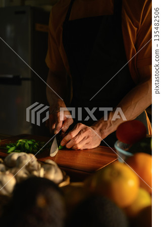 Cropped shot Man slicing green chili on a wooden board in a kitchen Cropped shot Man slicing green chili on a wooden board in a kitchen 135482506