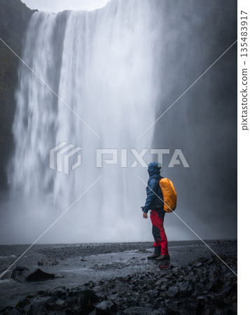 Vertical shot of hiker getting wet enjoying views on big waterfall in front of him, Iceland Vertical shot of hiker getting wet enjoying views on big waterfall in front of him, Iceland 135483917