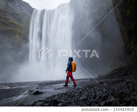 Vertical shot of hiker getting wet enjoying views on big waterfall in front of him, Iceland 135483920