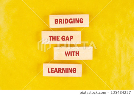 Four wooden blocks are stacked on a yellow surface. The blocks contain the red text bridging the gap with learning in capital letters 135484237