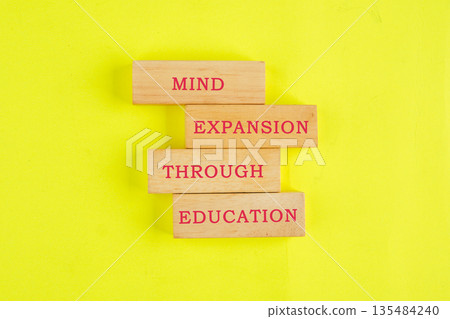 Four wooden blocks, each with red text, stack to say mind expansion through education. This is set against a bright yellow background Four wooden blocks, each with red text, stack to say mind expansion through education. This is set against a bright yellow background 135484240