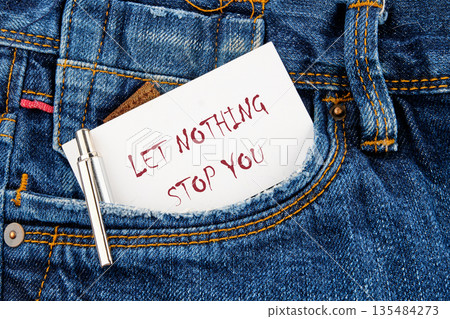 A handwritten card with the phrase Let Nothing Stop You is placed in a denim jean pocket next to a silver pen. The message conveys strength and motivation A handwritten card with the phrase Let Nothing Stop You is placed in a denim jean pocket next to a silver pen. The message conveys strength and motivation 135484273