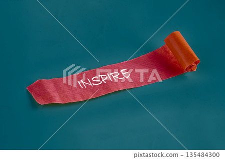 A crimson scroll, bearing the word INSPIRE, delicately unrolls against a tranquil, blue-green background, evoking feelings of possibility and fresh starts A crimson scroll, bearing the word INSPIRE, delicately unrolls against a tranquil, blue-green background, evoking feelings of possibility and fresh starts 135484300