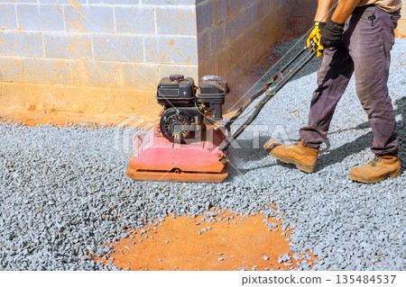 Worker uses compactor on gravel for construction site preparation Worker uses compactor on gravel for construction site preparation 135484537