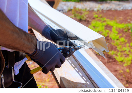 Worker cuts gutter vinyl siding on construction site with hand tools 135484539