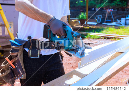 Work on construction vinyl siding with saw in hands at outdoor site with tools on belt 135484542