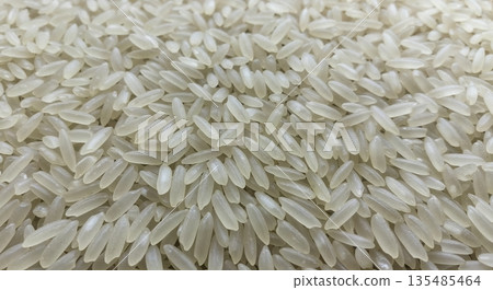 A full-frame close-up of numerous raw white jasmine rice grains creating a textured background, showcasing their elongated shape and translucent quality with soft, even lighting. A full-frame close-up of numerous raw white jasmine rice grains creating a textured background, showcasing their elongated shape and translucent quality with soft, even lighting. 135485464