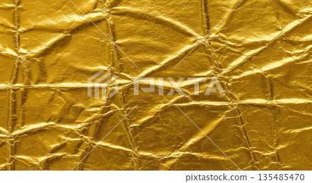 A vibrant macro texture of shiny crumpled gold foil paper creates an abstract background with intricate creases and reflective metallic surfaces. 135485470