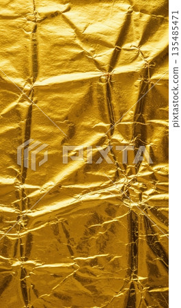 A vibrant macro texture of shimmering gold foil paper showcases intricate crinkles and reflective metallic folds, creating an abstract and luxurious background. 135485471