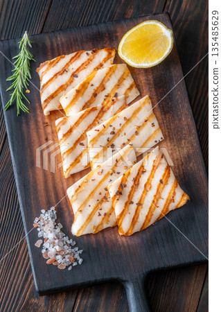 Grilled squid steaks with rosemary and lemon on dark wooden cutting board Grilled squid steaks with rosemary and lemon on dark wooden cutting board 135485629