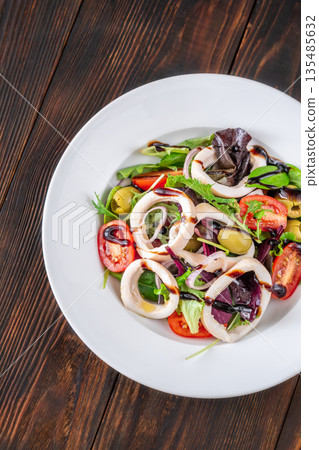Mediterranean squid salad with arugula olives and tomatoes on white ceramic plate 135485632
