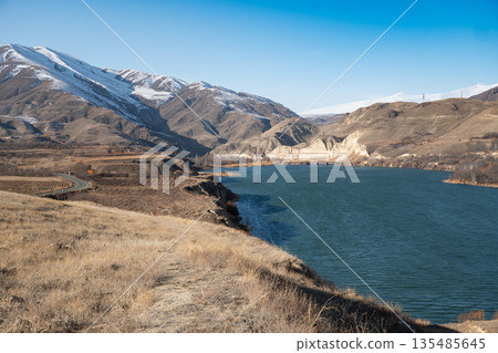 Shamb reservoir stretches between dry grassy shores and rugged mountains, blue water contrasts with warm earthy tones of the landscape Shamb reservoir stretches between dry grassy shores and rugged mountains, blue water contrasts with warm earthy tones of the landscape 135485645