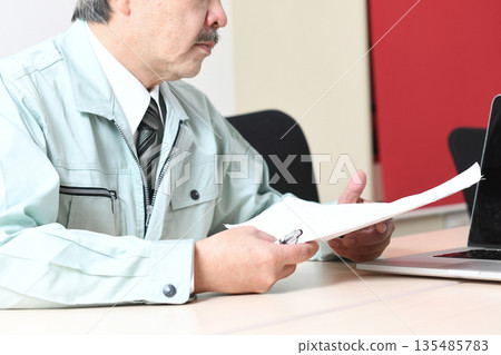 一位身著工作服的中年男子在商務會議期間查看文件。 135485783