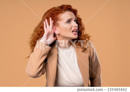 Ginger Woman Pointing To Ear With Confused Face, Signaling She Cant Hear Clearly Ginger Woman Pointing To Ear With Confused Face, Signaling She Cant Hear Clearly 135485842