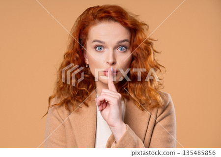 Beautiful businesswoman makes shush shh gesture with finger on lips, silence signaling Beautiful businesswoman makes shush shh gesture with finger on lips, silence signaling 135485856