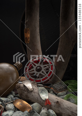 Vintage Soviet fishing gear with an old reel and predator lures placed on stones and wooden branches. 135486318