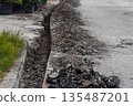 A shallow dug trench near the edge of an asphalt road with straight cut and hollowed-out edges. Works on replacement, maintenance, technical re-equipment of underground pipes and other communications 135487201