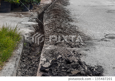 A shallow dug trench near the edge of an asphalt road with straight cut and hollowed-out edges. Works on replacement, maintenance, technical re-equipment of underground pipes and other communications A shallow dug trench near the edge of an asphalt road with straight cut and hollowed-out edges. Works on replacement, maintenance, technical re-equipment of underground pipes and other communications 135487201