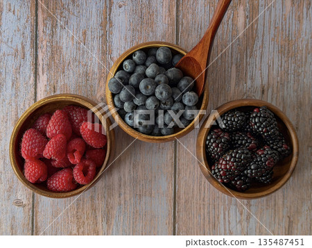 Fresh Raspberries, Blueberries, and Blackberries in Wooden Bowls with Spoon 135487451