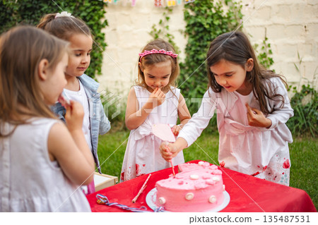 Children celebrate with pink cake at joyous garden party Children celebrate with pink cake at joyous garden party 135487531