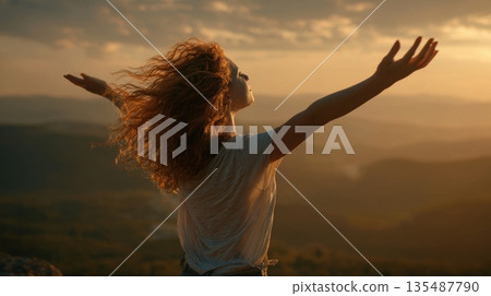 Woman standing on hilltop with arms open at sunset feeling freedom and inner peace 135487790