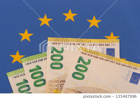 Euro banknotes against the flag of the European Union Euro banknotes against the flag of the European Union 135487896