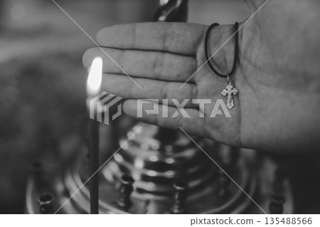 Baptism cross in a mans hand in front of candles, black and white photo Baptism cross in a mans hand in front of candles, black and white photo 135488566