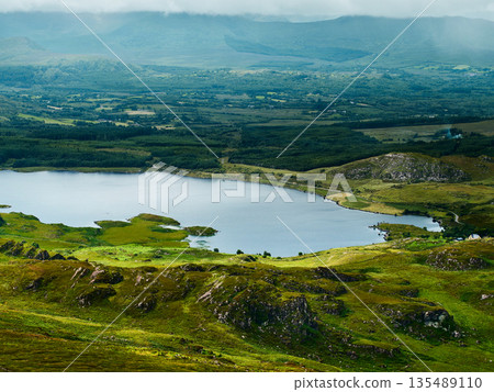 Viewing peaceful Lough and green countryside from rocky hillside during daytime. Viewing peaceful Lough and green countryside from rocky hillside during daytime. 135489110