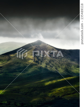 Dramatic landscape of mountains with dark storm clouds and sunbeams shining through. Dramatic landscape of mountains with dark storm clouds and sunbeams shining through. 135489118