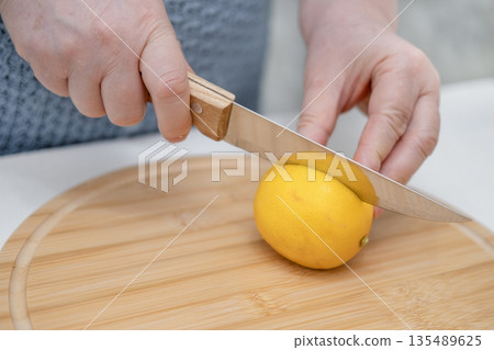 A woman's hands cut a lemon with a knife on a wooden board 135489625