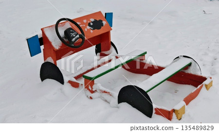 Toy Car Sled in Snow. Colorful wooden toy car sled covered in fresh snow. Winter playground object and seasonal toy. 135489829