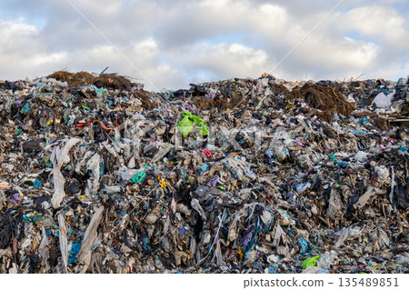 A large landfill site shows heaps of garbage and trash spread across the ground under a cloudy sky A large landfill site shows heaps of garbage and trash spread across the ground under a cloudy sky 135489851