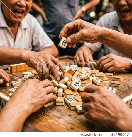 A lively group of older men laugh and socialize while playing a game of mahjong, a classic and beloved pastime. A close-up on hands and tiles captures the action.. High quality photo 135490067