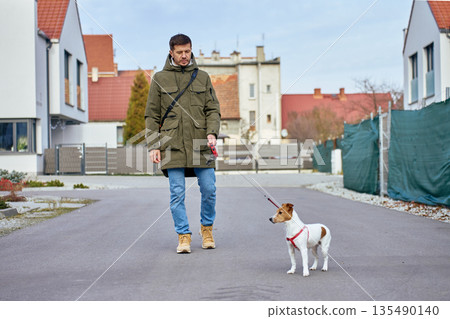 Man walking small dog on leash on quiet suburban street between residential houses Man walking small dog on leash on quiet suburban street between residential houses 135490140