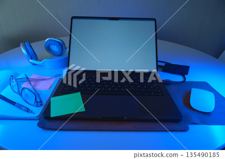 Laptop, headphones, and glasses on desk with blue light Laptop, headphones, and glasses on desk with blue light 135490185