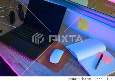 Modern workspace with laptop and notebook under neon lights 135490192