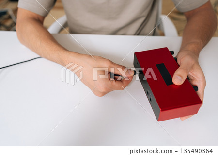 Top view of sound engineer connecting usb cable into portable audio interface, illustrating setup of digital device for music production, sound recording, modern studio connectivity on white table. 135490364