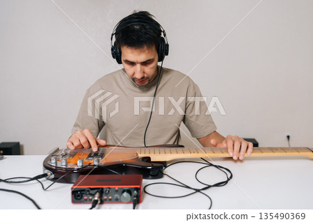 Portrait of musician male recording bass guitar using audio interface and headphones, creating music in home studio, focusing on sound engineering and musical composition, isolated background. 135490369