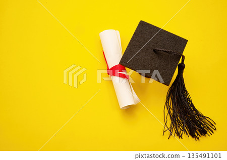 Graduation cap and diploma scroll on yellow background Graduation cap and diploma scroll on yellow background 135491101