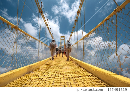 Tourists walking on yellow suspension bridge under blue sky Tourists walking on yellow suspension bridge under blue sky 135491819