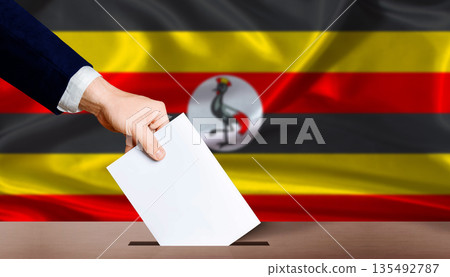 Hand placing a ballot in ballot box with the Ugandan flag in the background. Uganda presidential vote 135492787