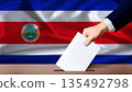 Hand placing a ballot in ballot box with the Costa Rican flag in the background. Costa Rica presidential vote 2026 135492798