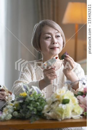 Senior woman arranging flowers as a hobby in the living room. Natural light 135492811